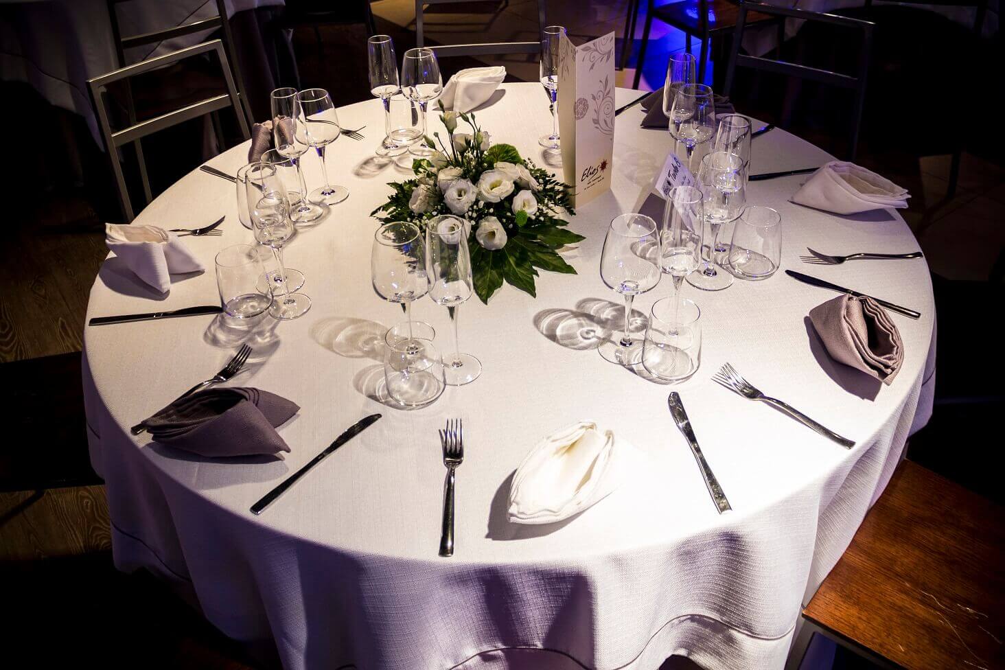 Tavolo apparecchiato con tovaglia bianca e tovaglioli bianchi e grigi. Centrotavola ed eleganti bicchieri completano la mise en place